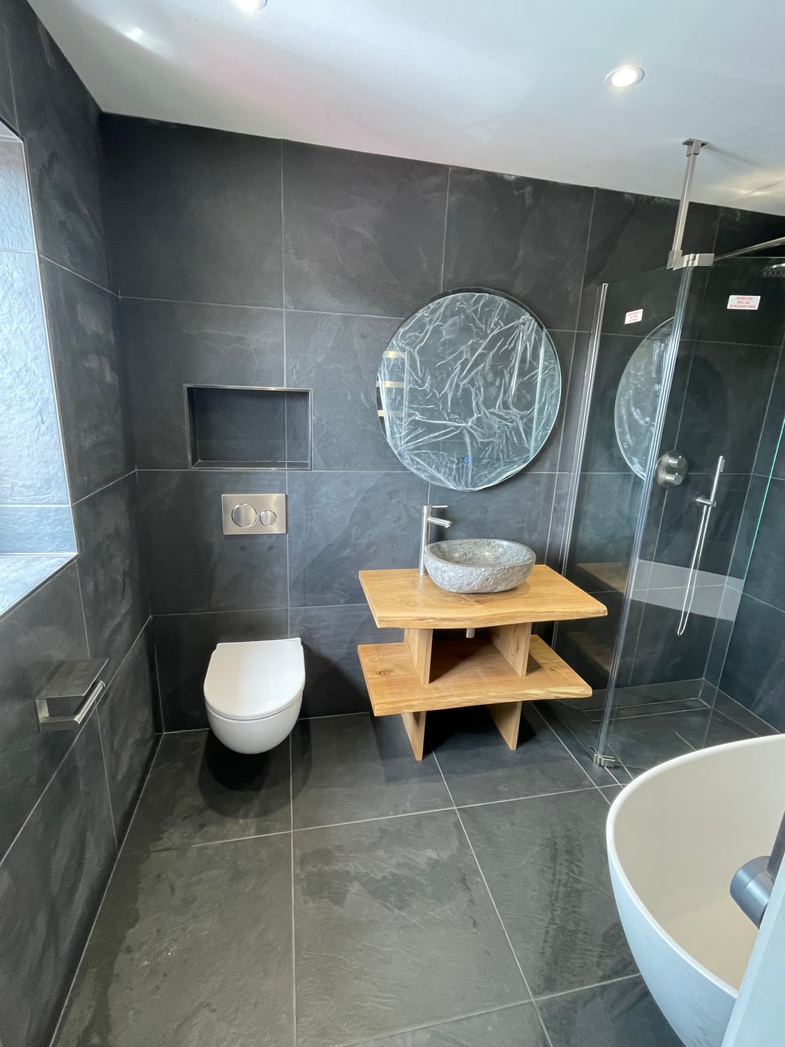 Completed dark-tiled bathroom with walk-in shower and timber vanity