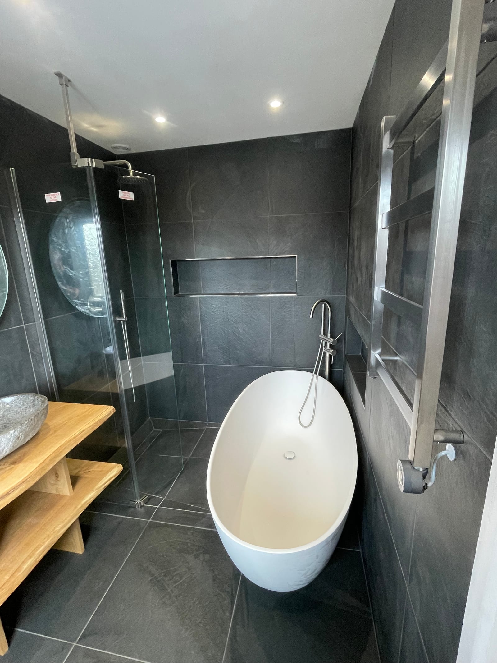 Freestanding bath and walk-in shower in a dark-tiled bathroom