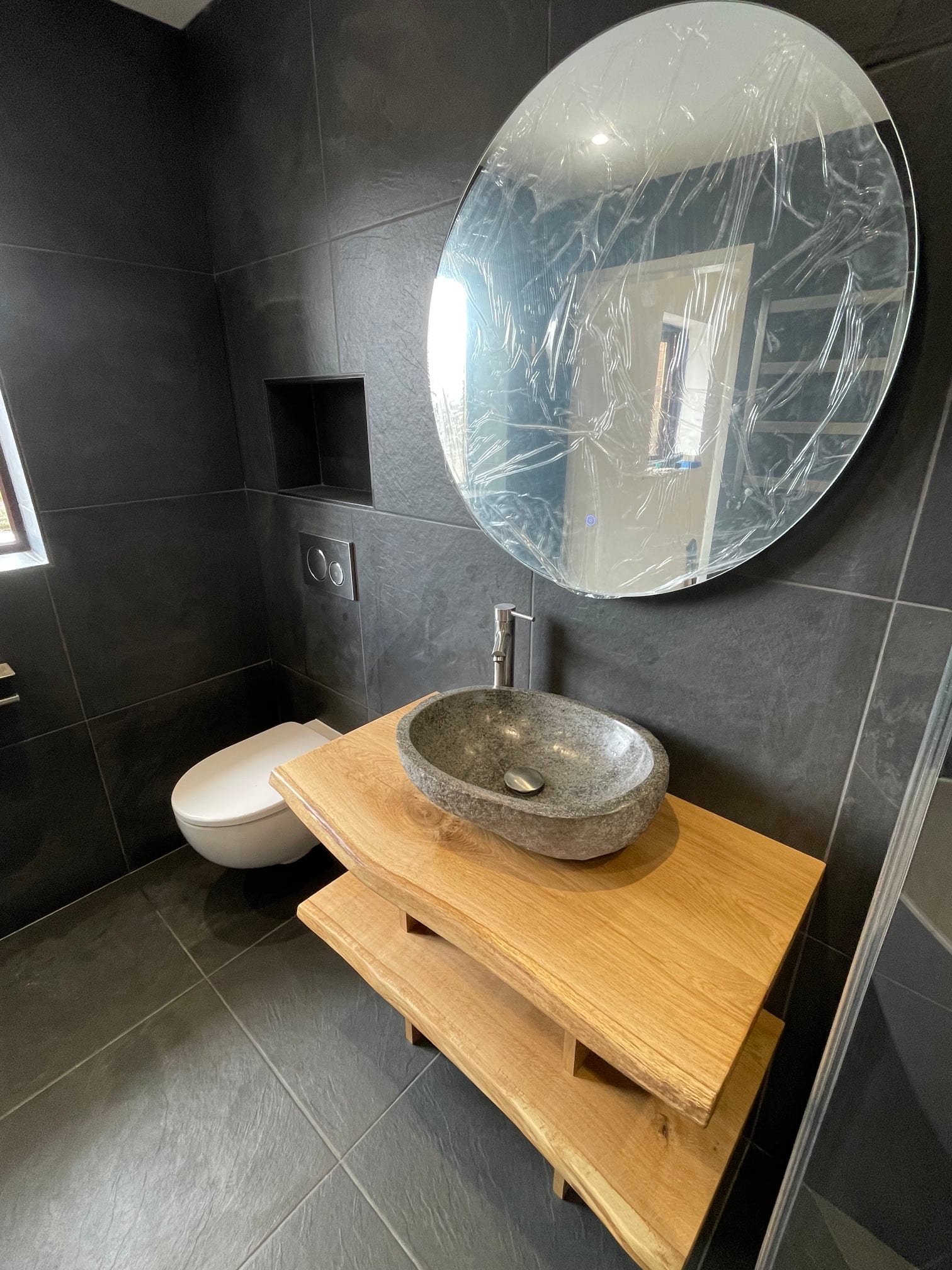 Stone basin on a timber vanity in a dark-tiled bathroom
