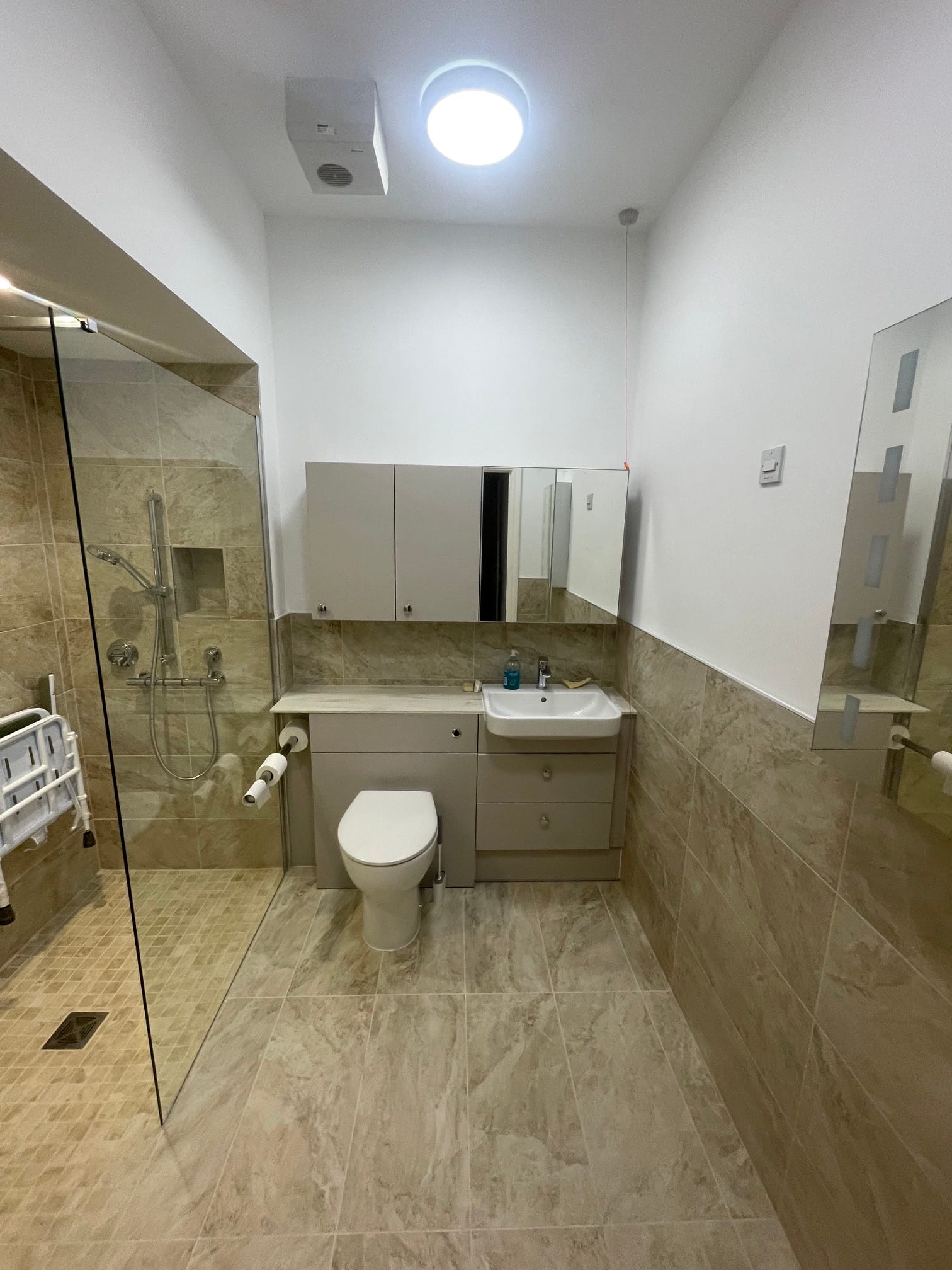 Light-tiled wet room with a glass shower screen and fitted vanity