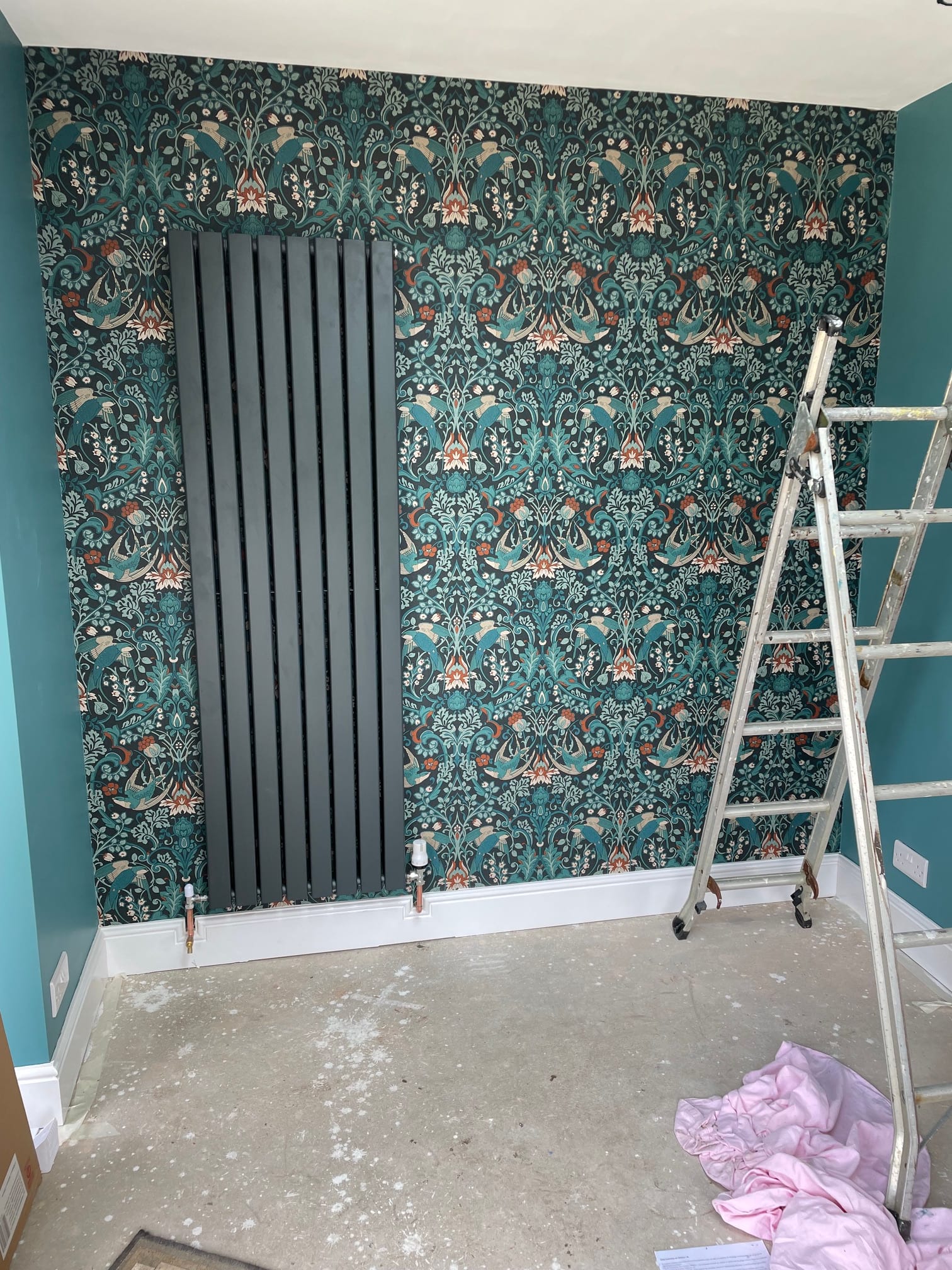 Tall dark radiator installed against patterned wallpaper